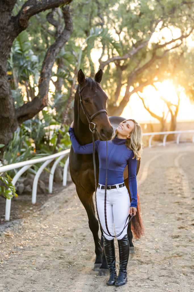 equestrian in riding outfit with bay horse in sunset
