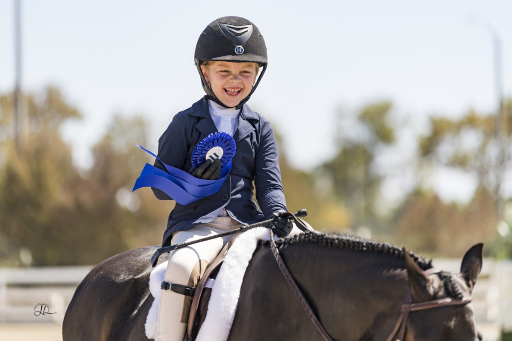 girl smiling with blue ribbon on her pony